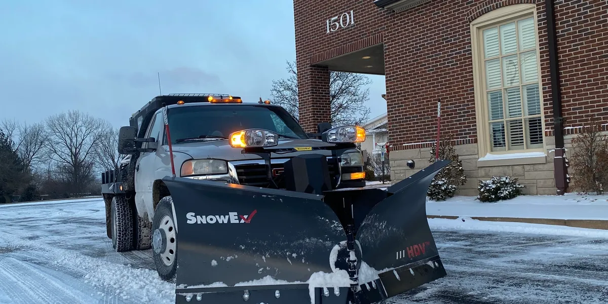 Professional snow removal service in St. Louis, MO with Porter's Lawn Service truck equipped with snow plow attachment clearing snow from roadway